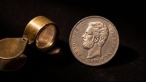 Home reales 13 Moneda De 5 Pesetas De Plata De Amadeo I De 1871, Con Una Lupa Antigua Sobre Fondo Oscuro
