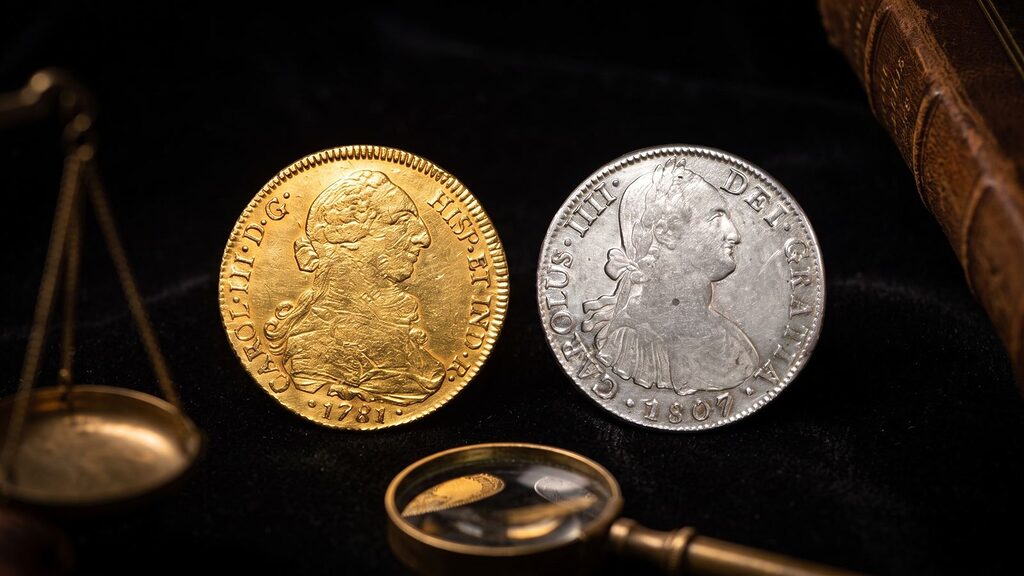 8 escudos de oro de Carlos III y 8 reales de plata de Carlos IV, comparados sobre fondo oscuro